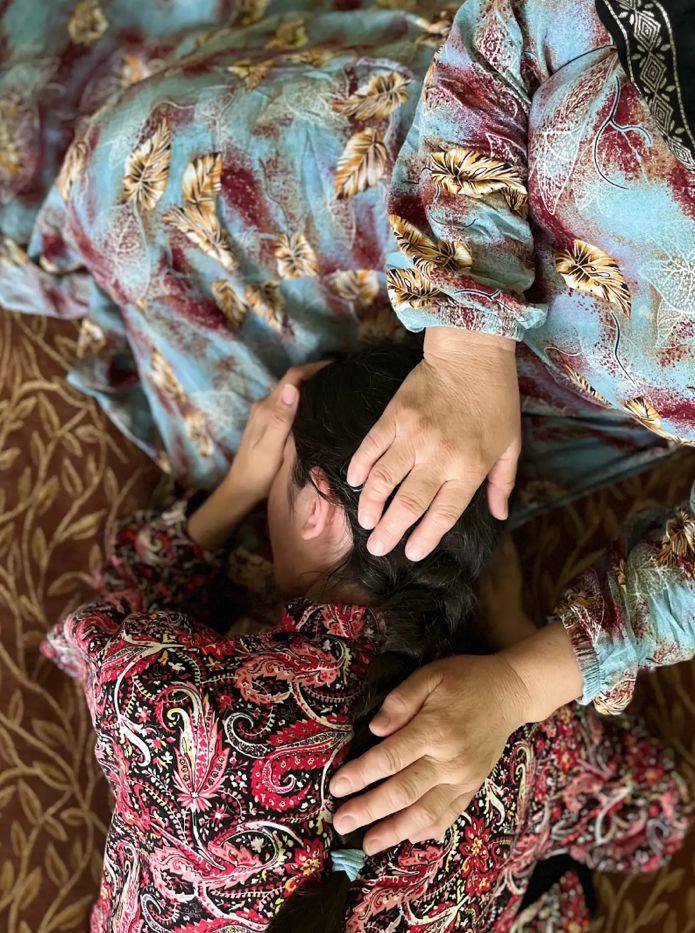 A person rests their head in another person’s lap, with hands resting gently on their head and back.